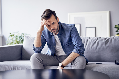 Besorgter, nachdenklicher Mann sitzt auf dem Sofa, lizenzfreies Stockfoto