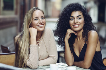 Portrait of two friends sitting in sidewalk cafe watching something - JSMF00052