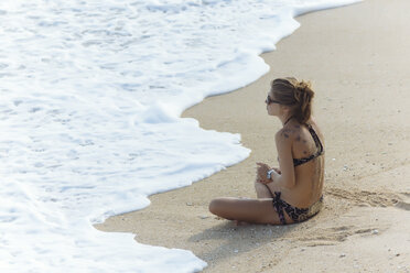 Indonesien, Bali, junge Frau sitzt am Strand - KNTF01057