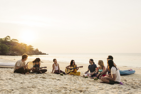 Thailand, Koh Phangan, Gruppe von Menschen sitzen am Strand mit Gitarre bei Sonnenuntergang, lizenzfreies Stockfoto