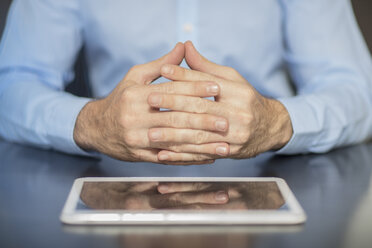 Man sitting at office desk with tablet folding hands - ZEF15100