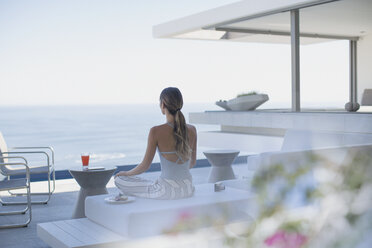 Gelassene Frau meditiert auf einer modernen, luxuriösen Musterhaus-Terrasse mit Meerblick - HOXF01030