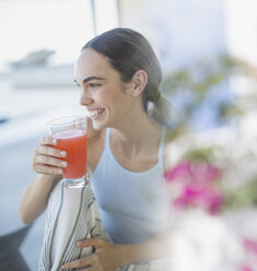 Smiling brunette woman in pajamas drinking juice - HOXF01038