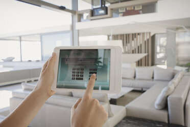 Personal perspective woman with digital tablet managing digital security system in modern, luxury home showcase interior living room - HOXF01039