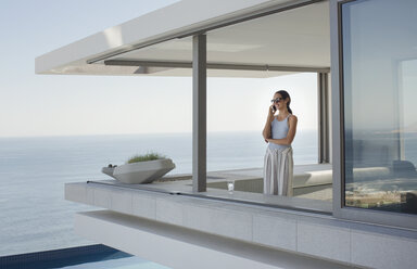 Frau, die auf einer modernen, luxuriösen Wohnung mit Blick auf das Meer telefoniert - HOXF01044