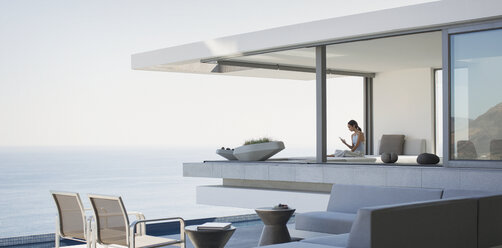Woman sitting on modern, luxury home showcase exterior patio with ocean view - HOXF01047