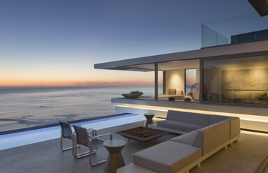 Illuminated modern, luxury home showcase exterior patio with sofa and lap pool with ocean view at dusk - HOXF01058