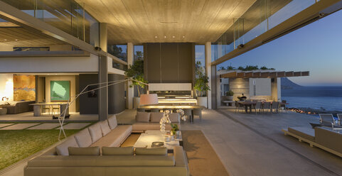 Illuminated modern, luxury home showcase interior living room open to patio at dusk - HOXF01062