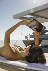 Frau beim Sonnenbaden, mit digitalem Tablet auf Liegestuhl auf sonniger Terrasse - HOXF01079