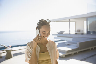 Lächelnde Frau, die auf einer sonnigen, modernen und luxuriösen Terrasse mit einem Smartphone telefoniert - HOXF01085