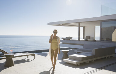 Frau im Badeanzug, die auf einer sonnigen, modernen, luxuriösen Musterhaus-Terrasse mit Meerblick spazieren geht - HOXF01089