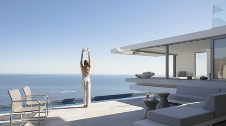 Frau übt Yoga-Berg-Pose auf sonnigen modernen, luxuriösen Haus Schaufenster Außenterrasse mit Meerblick - HOXF01097