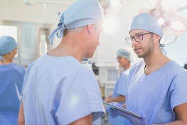 Männliche Chirurgen mit digitalem Tablet im Gespräch im Operationssaal - HOXF01100