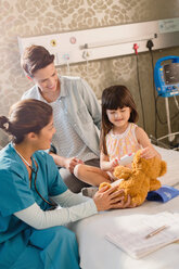 Eine Krankenschwester und ein Mädchen benutzen ein digitales Thermometer an einem Teddybären in einem Krankenhauszimmer - HOXF01101