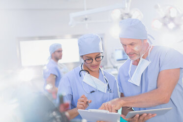 Chirurgen mit digitalem Tablet besprechen Papierkram auf einem Klemmbrett im Operationssaal - HOXF01103