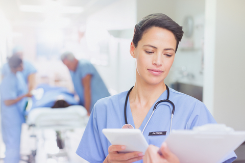 Chirurgin mit digitalem Tablet, die in einem Krankenhauskorridor Papierkram am Klemmbrett überprüft, lizenzfreies Stockfoto
