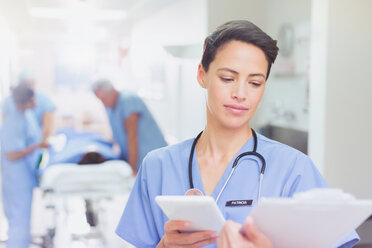 Female surgeon with digital tablet reviewing clipboard paperwork in hospital corridor - HOXF01104