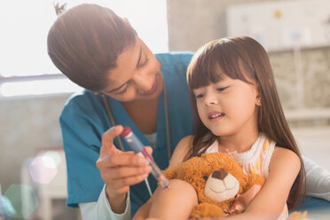 Female nurse teaching girl patient with teddy bear how to use insulin pen - HOXF01108