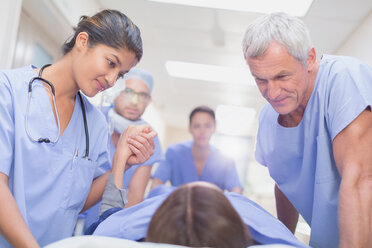 Pflegende Chirurgen im Gespräch mit einem Patienten auf einer Bahre im Krankenhausflur - HOXF01112