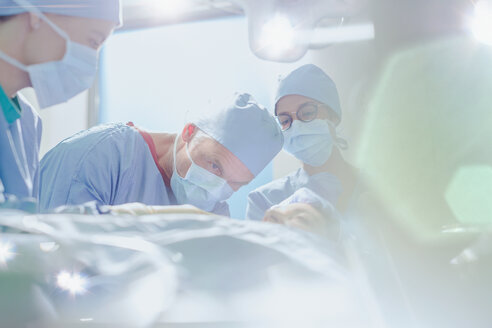 Fokussierter männlicher Chirurg bei einer Operation an einer Patientin im Operationssaal - HOXF01114