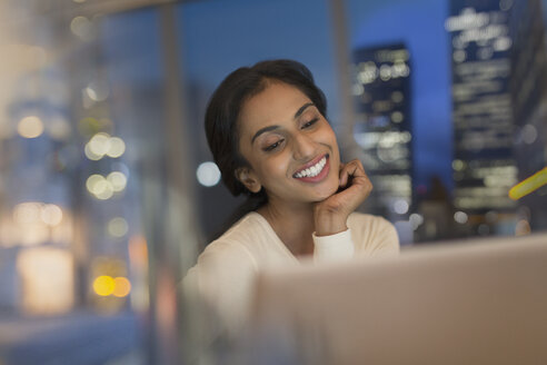 Lächelnde Geschäftsfrau, die nachts im Büro am Laptop arbeitet - HOXF01145