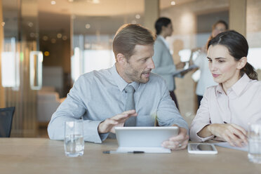 Geschäftsmann und Geschäftsfrau, die ein digitales Tablet benutzen und sich in einem Konferenzraum unterhalten - HOXF01156