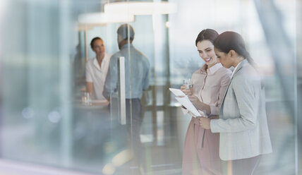 Businesswomen talking, reviewing paperwork in office - HOXF01159