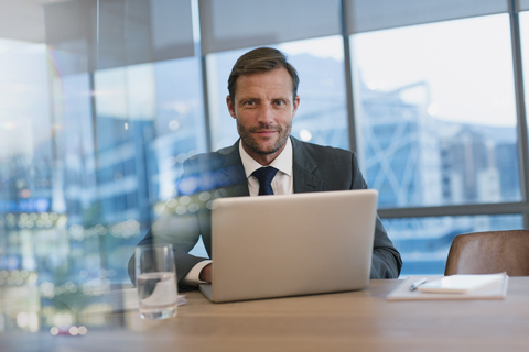 Porträt eines seriösen Geschäftsmannes, der in einem Konferenzraum am Laptop arbeitet, lizenzfreies Stockfoto