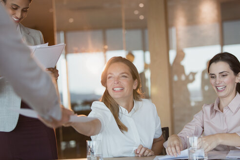 Lächelnde Geschäftsfrau, die einem Kollegen in einem Konferenzraum Papierkram übergibt - HOXF01167
