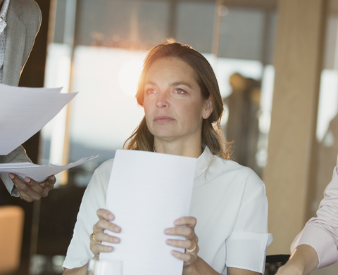 Ernste, nachdenkliche Geschäftsfrau mit Papierkram, die im Büro wegschaut, lizenzfreies Stockfoto
