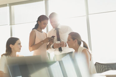 Business people texting with cell phones in sunny conference room meeting - HOXF01179