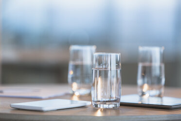Water in glasses next to digital tablets on table - HOXF01184