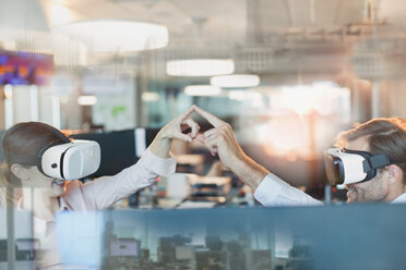 Computer programmers using virtual reality simulator glasses, touching fingers in office - HOXF01188