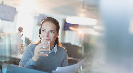 Geschäftsfrau mit Headset trinkt Wasser im Büro - HOXF01193