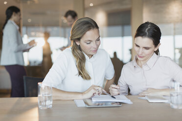 Businesswomen reviewing paperwork in conference room meeting - HOXF01204