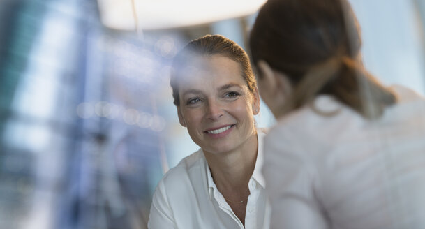 Lächelnde Geschäftsfrau hört einem Kollegen zu - HOXF01214