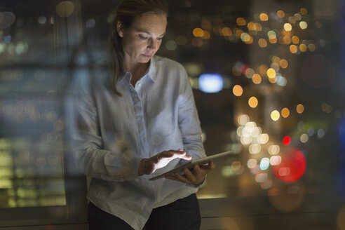 Businesswoman working late at digital tablet in office at night - HOXF01245