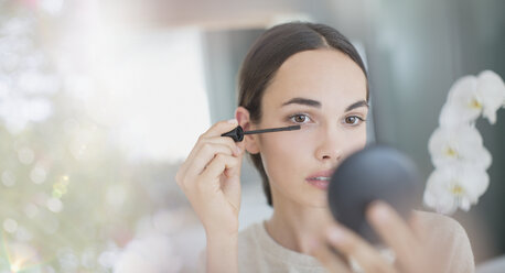 Woman apply mascara with mascara wand and compact mirror - HOXF01250