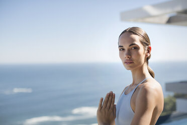 Portrait serene woman practicing yoga with hands at heart center on sunny patio with ocean view - HOXF01255