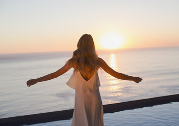 Woman with arms outstretched watching tranquil sunset view over ocean horizon - HOXF01264