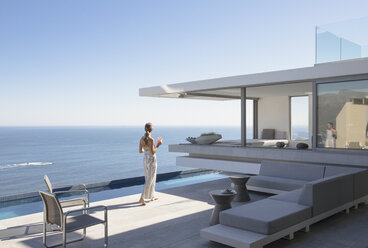 Woman on sunny modern, luxury home showcase exterior patio with ocean view - HOXF01272