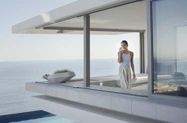 Frau, die auf einer modernen, luxuriösen Wohnung mit Blick auf den Ozean telefoniert - HOXF01275