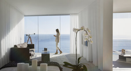 Frau steht auf dem Balkon eines modernen Luxushauses mit sonnigem Meerblick - HOXF01279