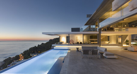 Illuminated modern, luxury home showcase exterior patio with lap pool and ocean view at twilight - HOXF01281