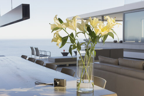 Gelber Lilienstrauß in Vase auf modernem, luxuriösem Home Showcase Interieur Esstisch neben Digitalkamera - HOXF01329
