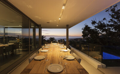 Beleuchteter Terrassentisch aus Holz mit Gedecken in der Abenddämmerung - HOXF01335