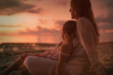 Serene mother and daughter relaxing on beach at dusk - HOXF01374