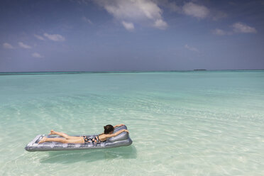 Mädchen, das auf einem aufblasbaren Floß im tropischen blauen Ozean liegt und schwimmt - HOXF01381