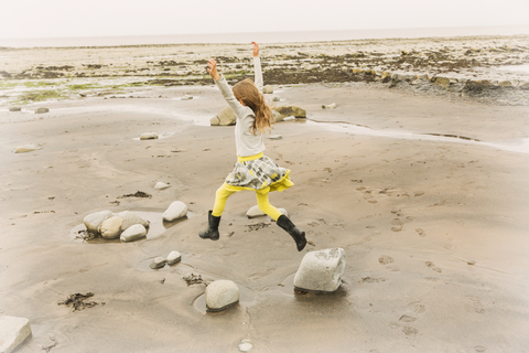 Übermütiges Mädchen springt vor Freude auf Strandfelsen, lizenzfreies Stockfoto