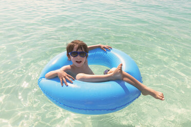 Porträt lächelnder Junge mit Sonnenbrille schwimmt in blauem aufblasbarem Ring im Meer - HOXF01391